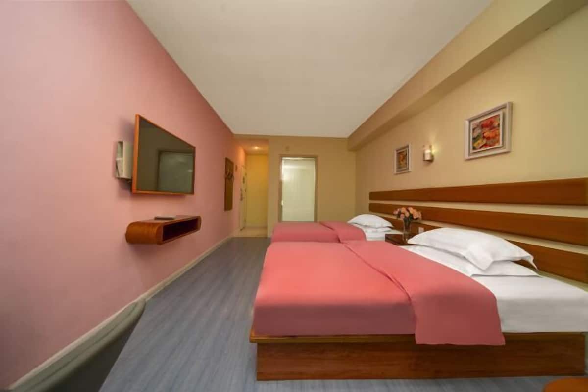 A hotel room with two beds, a wooden headboard, a mirror, and a framed picture on the wall.