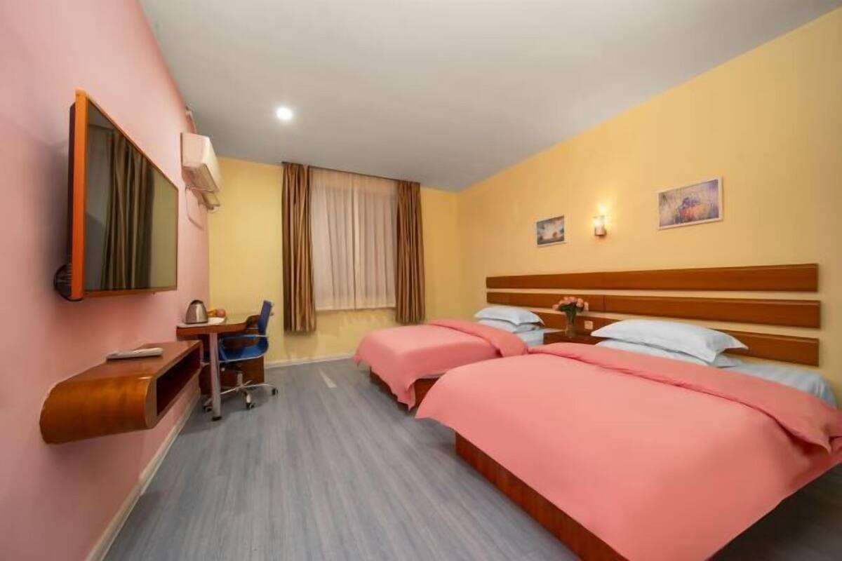 A hotel room with two beds, a desk, a chair, a mirror, and a window with curtains.