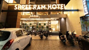 Außenansicht des Shree Ram Hotels mit einer Schautafel, einem Auto und mehreren parkenden Motorrädern.