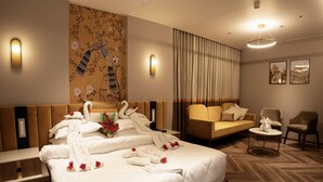 Ein Hotelzimmer mit einem großen Bett, einer Couch, einem kleinen Tisch und einem Sessel. Es gibt Wandleuchten und eine Deckenlampe.