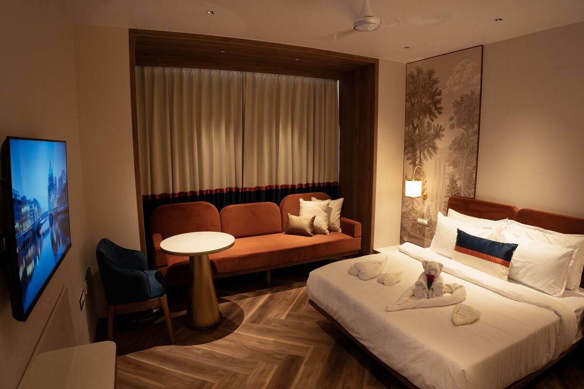 A hotel room with a bed, a sofa, a small table, and a TV.