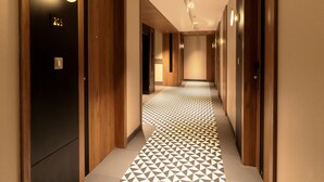 Ein Hotelkorridor mit Holztüren, einem gemusterten Boden und eingelassener Beleuchtung.