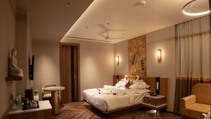 Ein modernes Hotelzimmer mit Holzboden im Fischgrätmuster, einem Bett mit weißen Leinentüchern, einem Nachttisch aus Holz, einem Schreibtisch mit Stuhl, einer Couch und einem an der Wand montierten Fernseher.