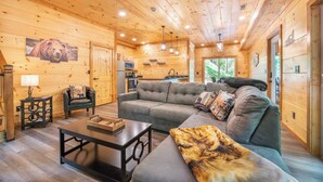 A cozy cabin interior with a wooden interior, a sofa, a coffee table, and a dining table. - Gorgeous 3BD Near Creek! Hot Tub + FirePit + Games (Sevierville)