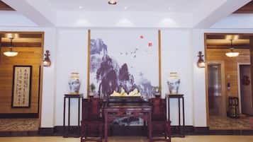 Um saguão com uma pintura tradicional chinesa, um piano e dois vasos em pedestais.