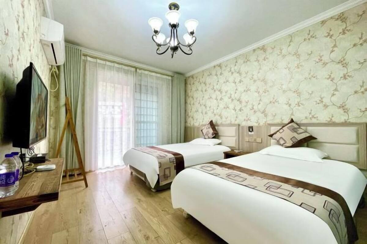 A hotel room with two beds, a TV, a desk, and a chandelier.