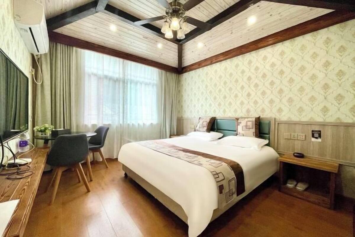 A hotel room with a large bed, a desk with a chair, and a small bedside table.