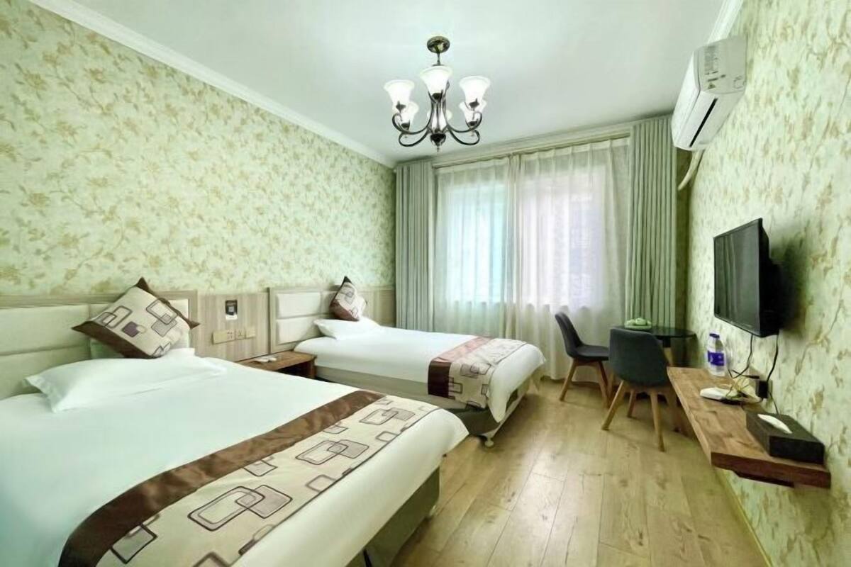 A hotel room with two beds, a desk, a chair, a TV, and a chandelier.