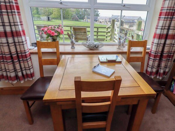 A wooden dining table with four chairs, a notebook, and a vase of flowers.
