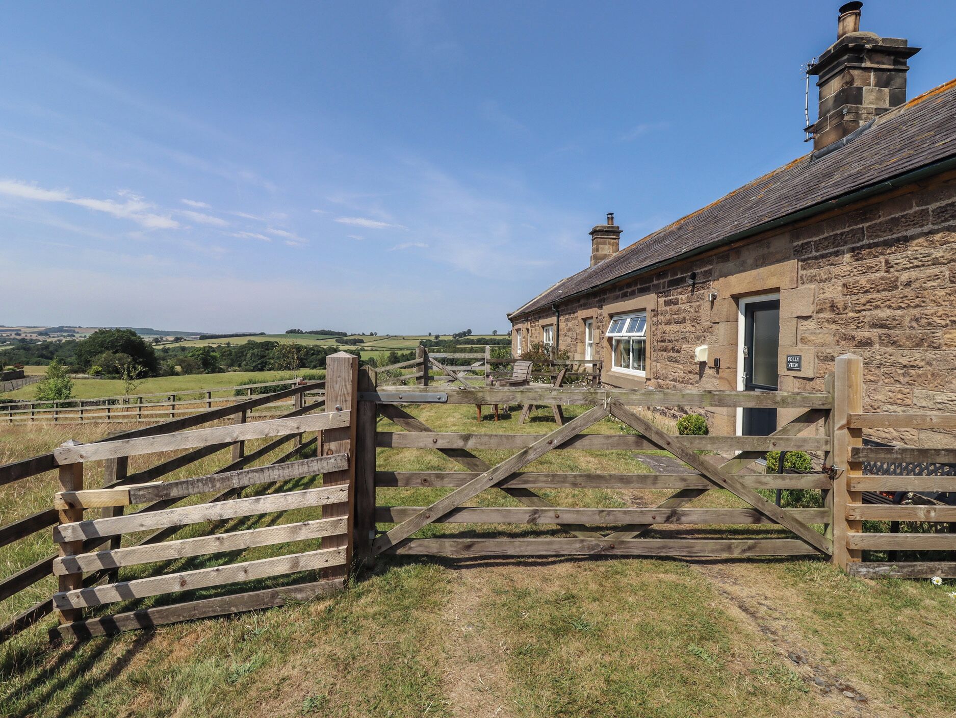 A stone building with a wooden gate, a view of the countryside, and a sign indicating 'Folly View.'