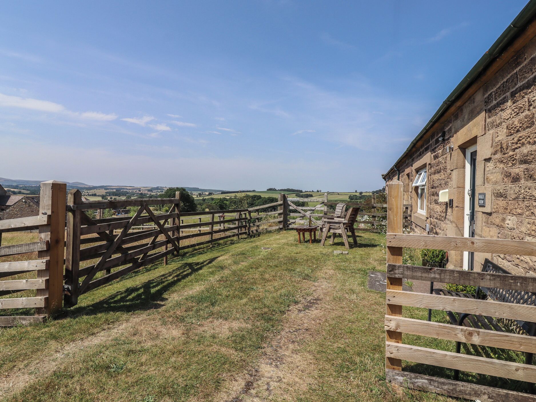 A rustic stone building with a wooden fence leading to a grassy path.