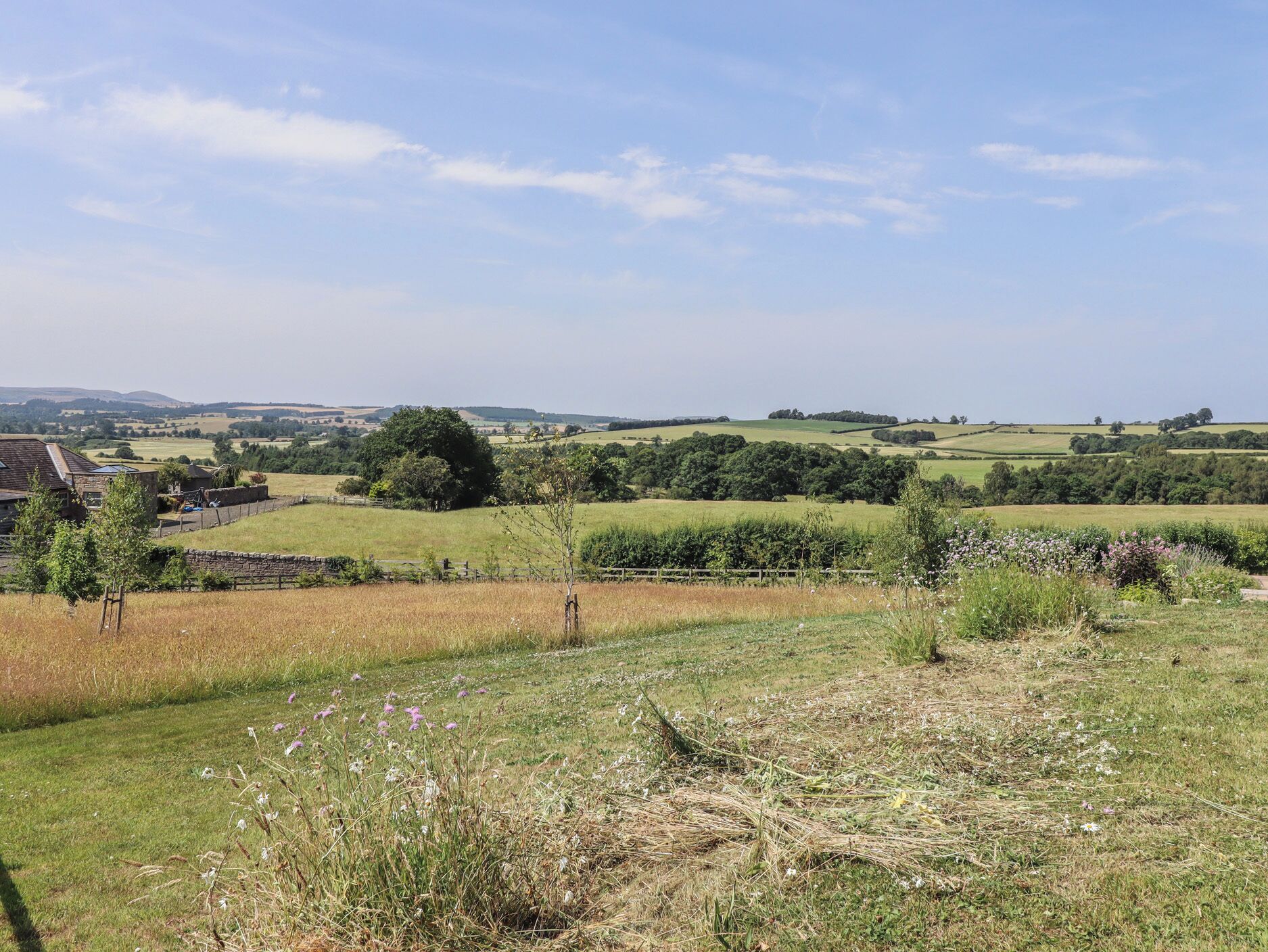 A rural landscape with rolling hills, a stone wall, and a stone building.