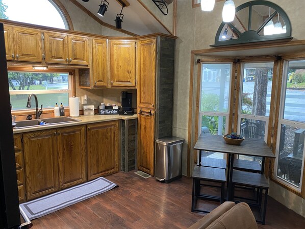 A kitchen with wooden cabinets, a stainless steel sink, a coffee maker, and a window overlooking a street.