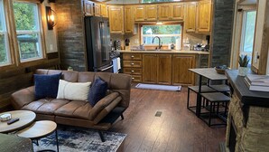 Ein gemütliches Wohnzimmer mit einer Ledersofa, einem Couchtisch und einem Teppich. Die Küche verfügt über Holzschränke, einen Kühlschrank und ein großes Fenster.