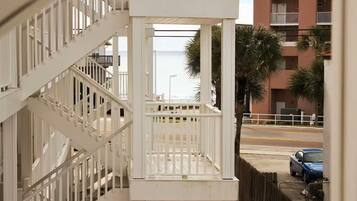 A white balcony with a view of a street and palm trees.