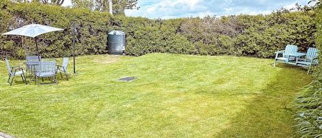 Un patio trasero bien cuidado con césped, una mesa con sillas, un depósito de agua y un seto.