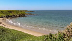 A coastal landscape with a sandy beach, grassy hills, and a clear blue sky.