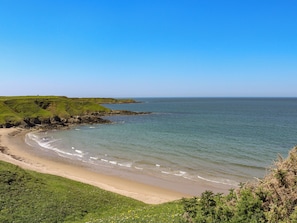 Un paysage côtier avec une plage de sable, des collines verdoyantes et un ciel bleu dégagé.