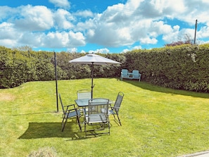 A grassy outdoor area with a table and chairs, a metal umbrella, and a hedge in the background. - 3 bedroom accommodation in Tudweiliog (Tudweiliog)