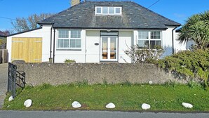 A white two-story house with a grey roof, a wooden garage door, and a stone wall.