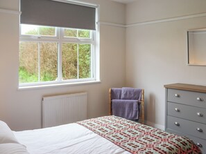 A bedroom with a bed, a dresser, a window with a view of greenery, and a radiator.
