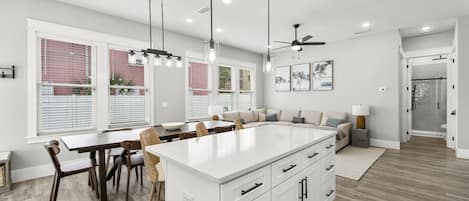 Une cuisine moderne dotée d’un grand îlot central, d’un coin repas avec des chaises et d’un espace salon intégré.
