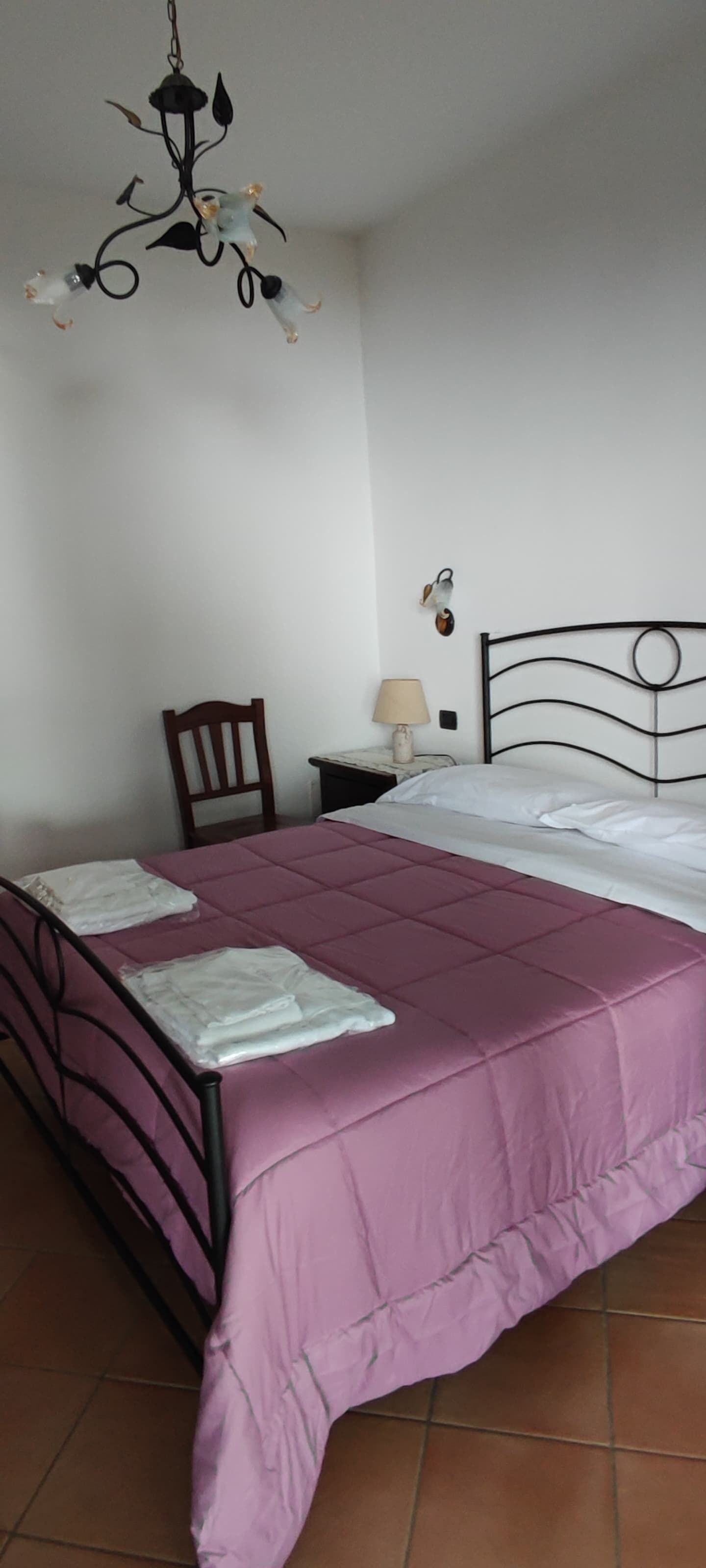 Un dormitorio con cama, mesita de noche, silla, lámpara y candelabro.