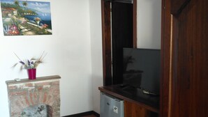 A room with a tiled floor, a small brick fireplace, a refrigerator, a wooden cabinet, and a painting on the wall. - AGRITURISMO  LA FOCAZZA (Ascea)