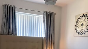 A bedroom with a bed, curtains, a bedside lamp, a radiator, and a wall decoration. - Spacious 3-Bedroom Family Home in Quiet Middleton | Minutes from Manchester City (Middleton)