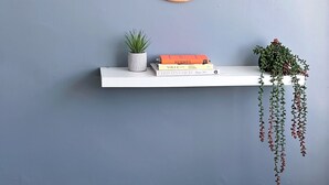 A room with a grey wall, a round mirror with a wooden frame, a white shelf with books and a small plant, and a beige sofa. - Spacious 3-Bedroom Family Home in Quiet Middleton | Minutes from Manchester City (Middleton)