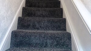 A staircase with carpeted steps leading to a landing where the word "HOME" is displayed. - Spacious 3-Bedroom Family Home in Quiet Middleton | Minutes from Manchester City (Middleton)