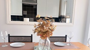 A dining table set with white plates, a clear glass vase with dried flowers, and a modern kitchen in the background. - Spacious 3-Bedroom Family Home in Quiet Middleton | Minutes from Manchester City (Middleton)