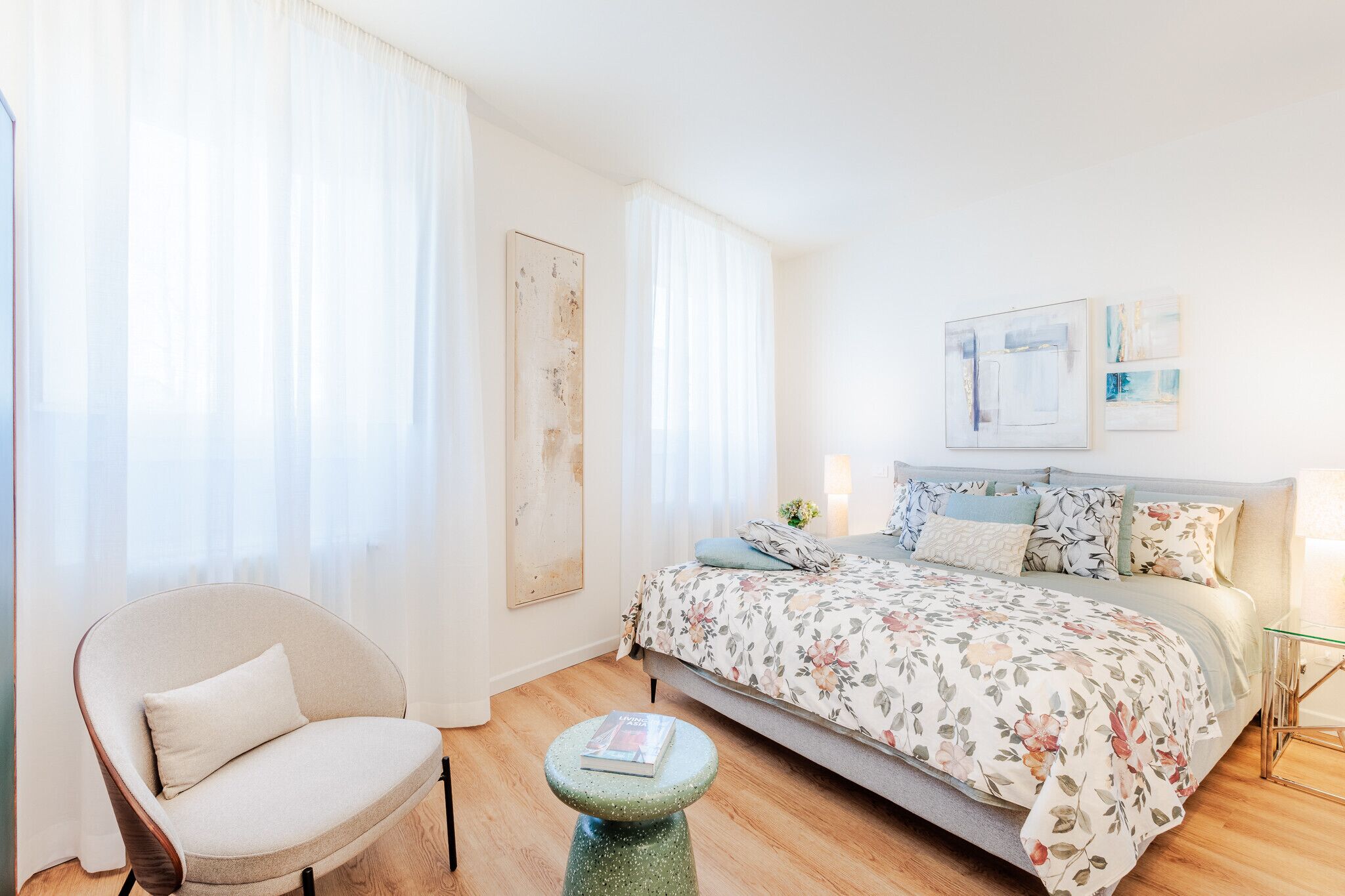 A bedroom with a bed, a chair, a small stool, and artwork on the wall.