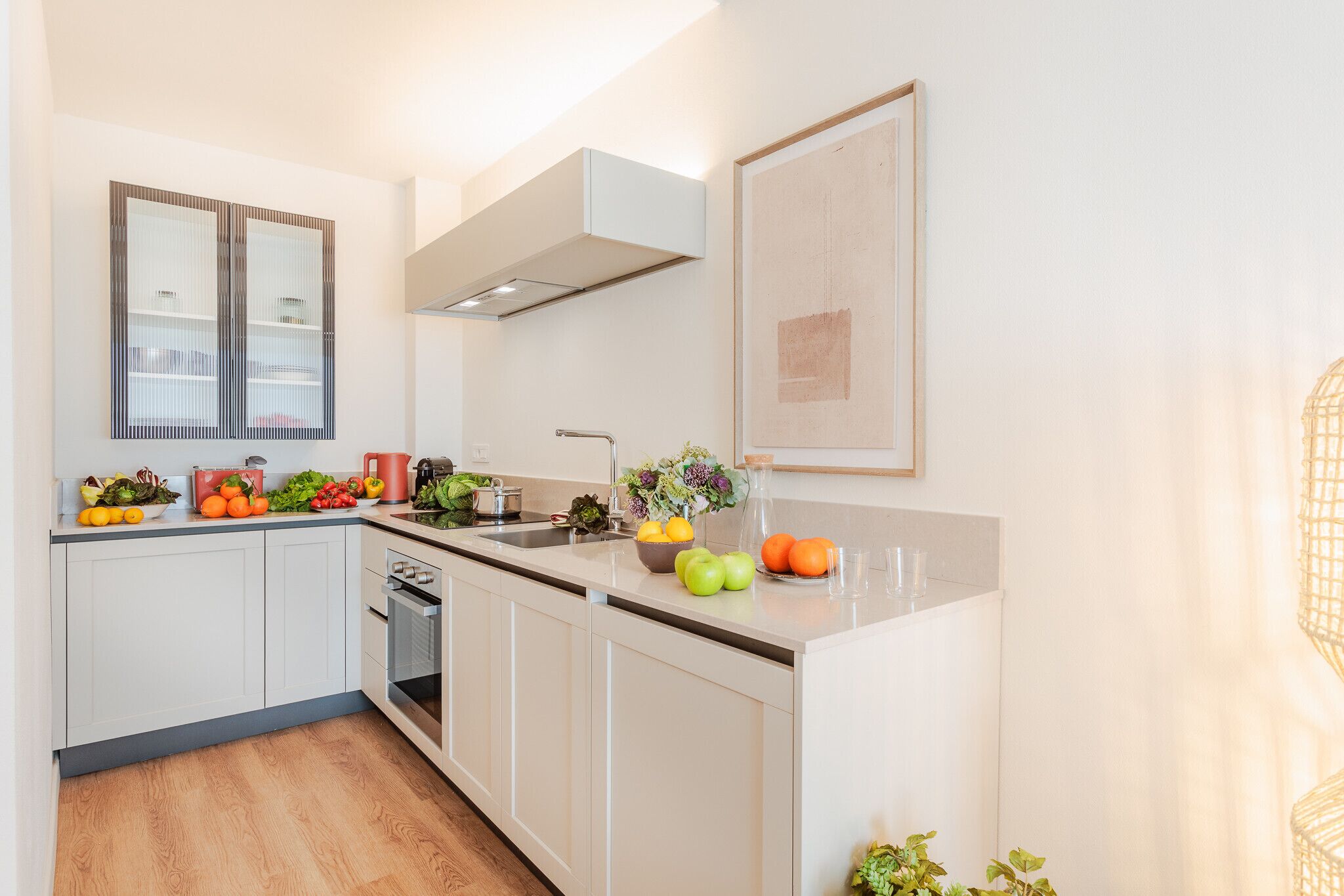 Una cocina moderna con armarios blancos, horno integrado y pileta de acero inoxidable.