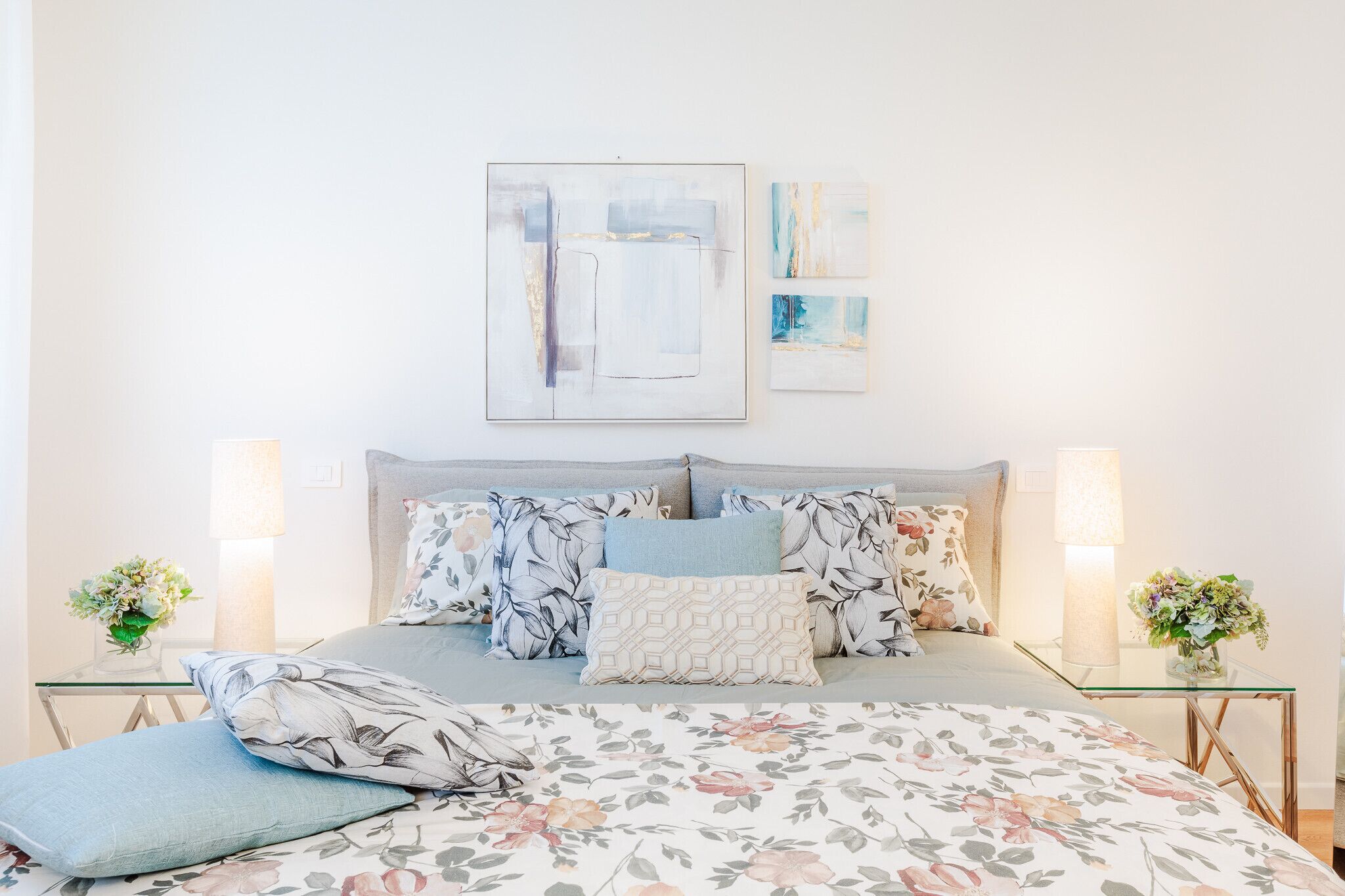 Une chambre à coucher avec un lit, une literie à motifs floraux et deux tables de chevet ornées de lampes et de fleurs.