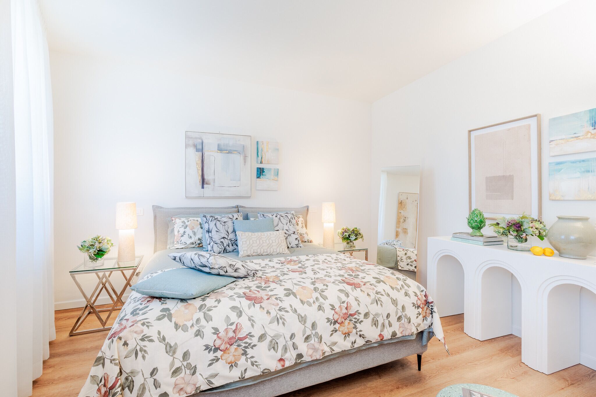 A bedroom with a floral bedspread, a bedside table with a lamp, and a dresser with decorative items.