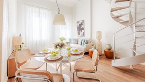A dining area with a round table, wicker chairs, and a white sofa. A spiral staircase is visible to the right. - Letizia Vista in Lucca (Lucca)