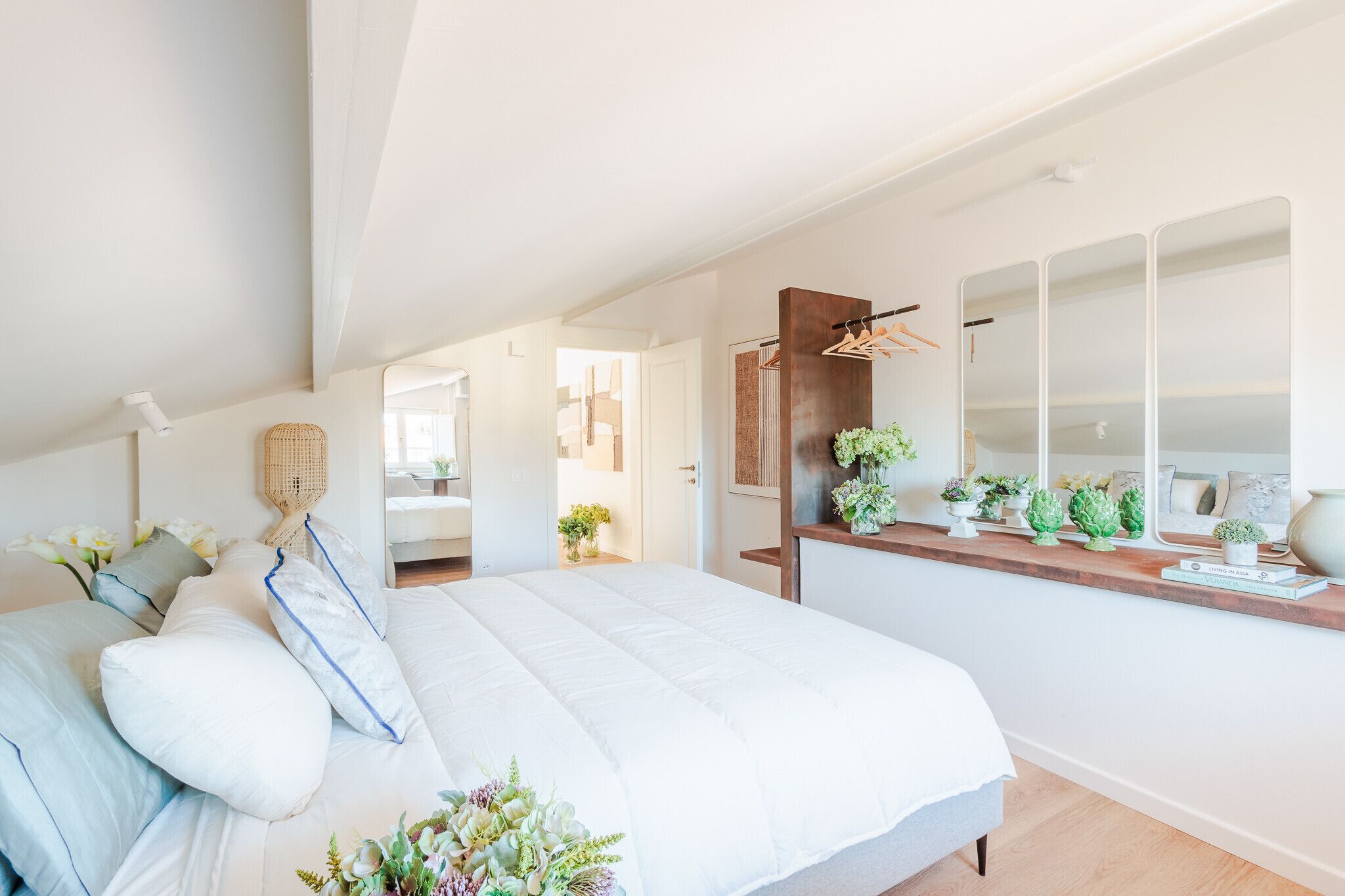 Un dormitorio moderno con una cama grande, una mesita de noche de madera con plantas, un espejo y un armario.
