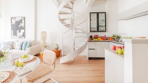 A modern kitchen with a white spiral staircase, a dining area with a table set for two, and a living room with a sofa and decorative pillows. - Letizia Vista in Lucca (Lucca)