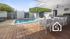 Ein überdachter Außenbereich mit Pool, Grill und Esstisch mit Stühlen.