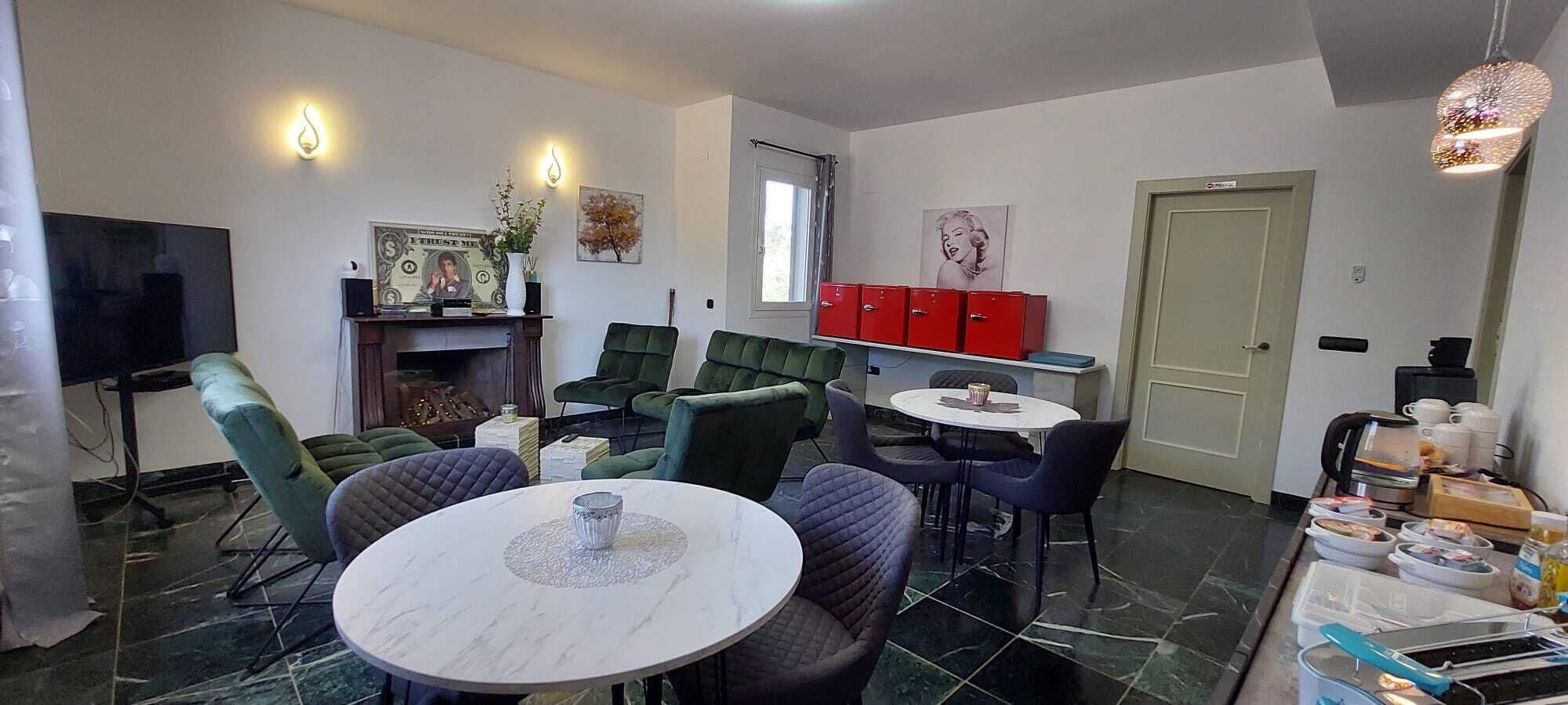 Un salón con chimenea, sillas verdes, una mesa de comedor y armarios rojos.