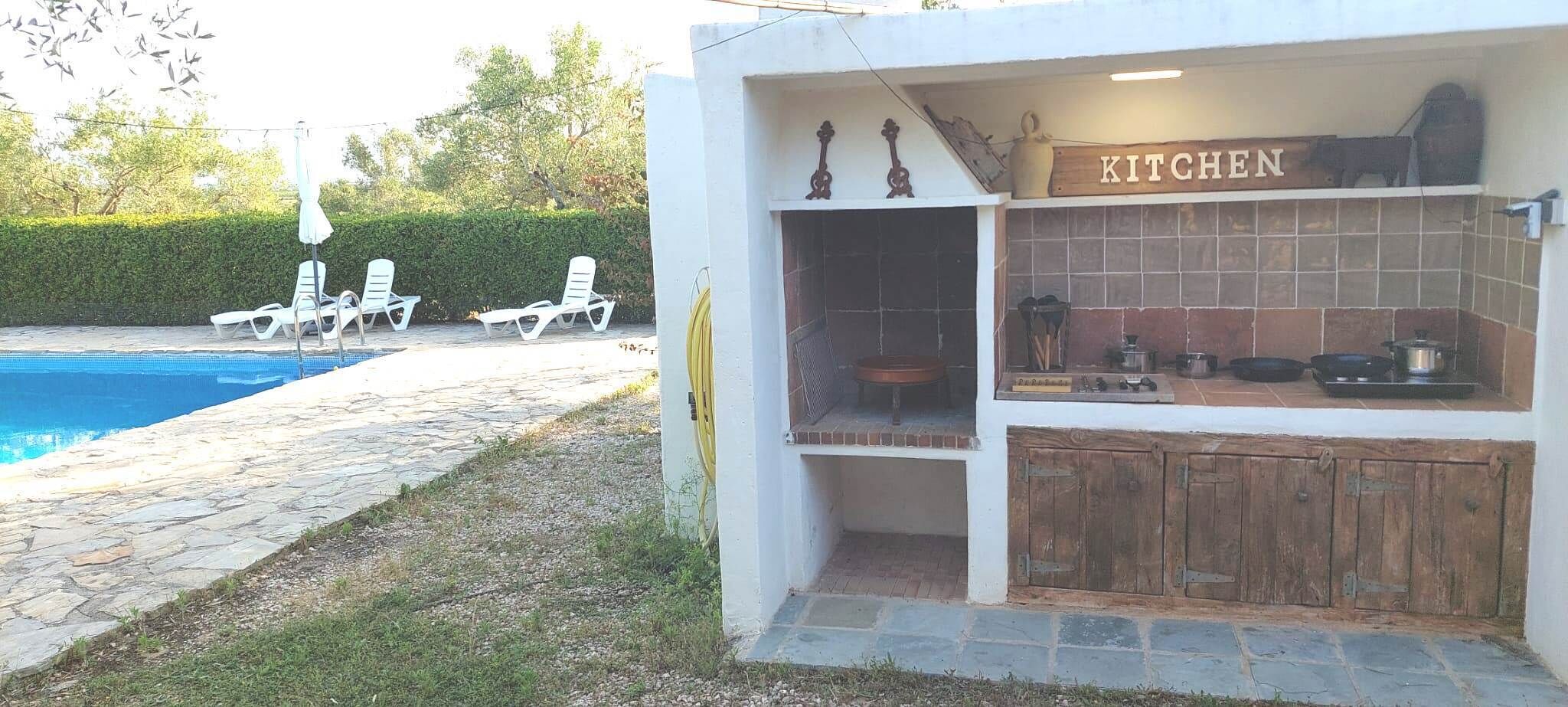 Una cocina al aire libre pequeña con un letrero que dice 'KITCHEN', una piscina y sillas de descanso.