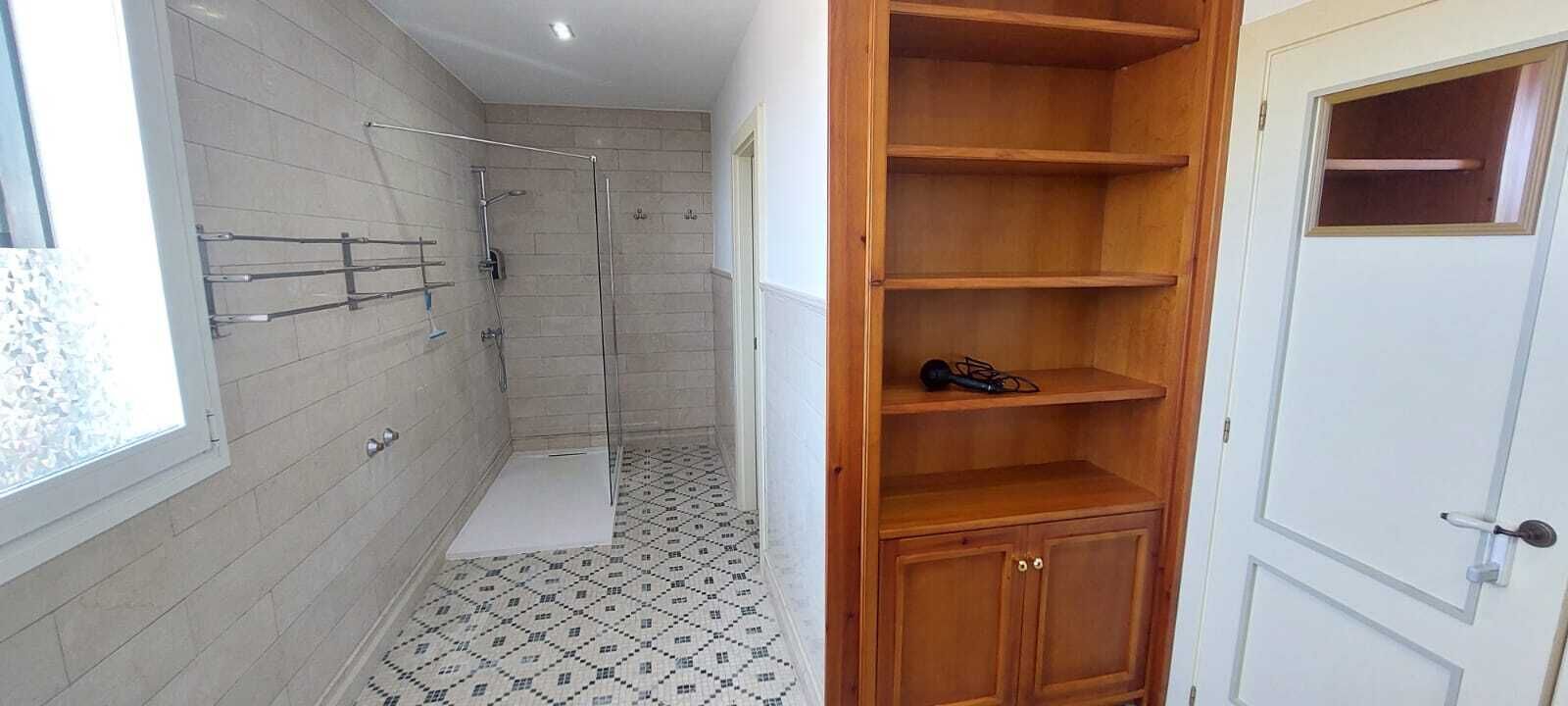 A bathroom with a shower, tiled floor, and a wooden shelf unit.