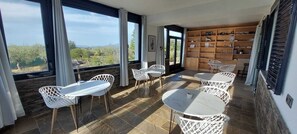 A sunlit room with a view, white wicker furniture, and a wooden shelf with various items. - Villa Pardalot Boutique Stays (Calig)