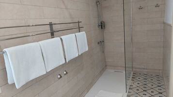 A modern bathroom with a glass shower enclosure, a towel rack with three towels, and a patterned floor.