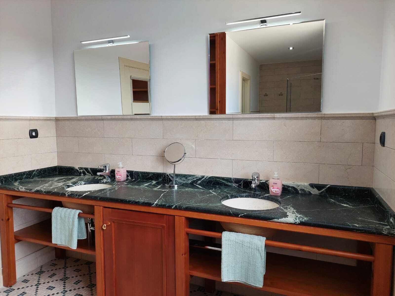 Un baño con tocador de mármol, dos lavabos, un espejo y un perchero para toallas.