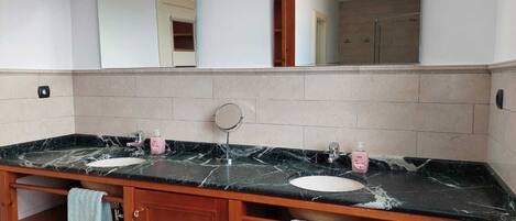 Un baño con tocador de mármol, dos lavabos, un espejo y un perchero para toallas.