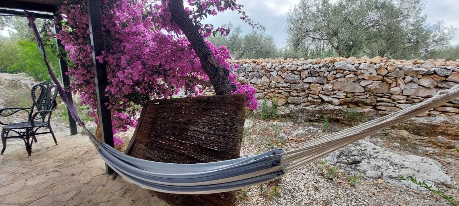 Un hamac sous une pergola ornée de fleurs roses, un mur de pierre et un coin salon extérieur rustique.