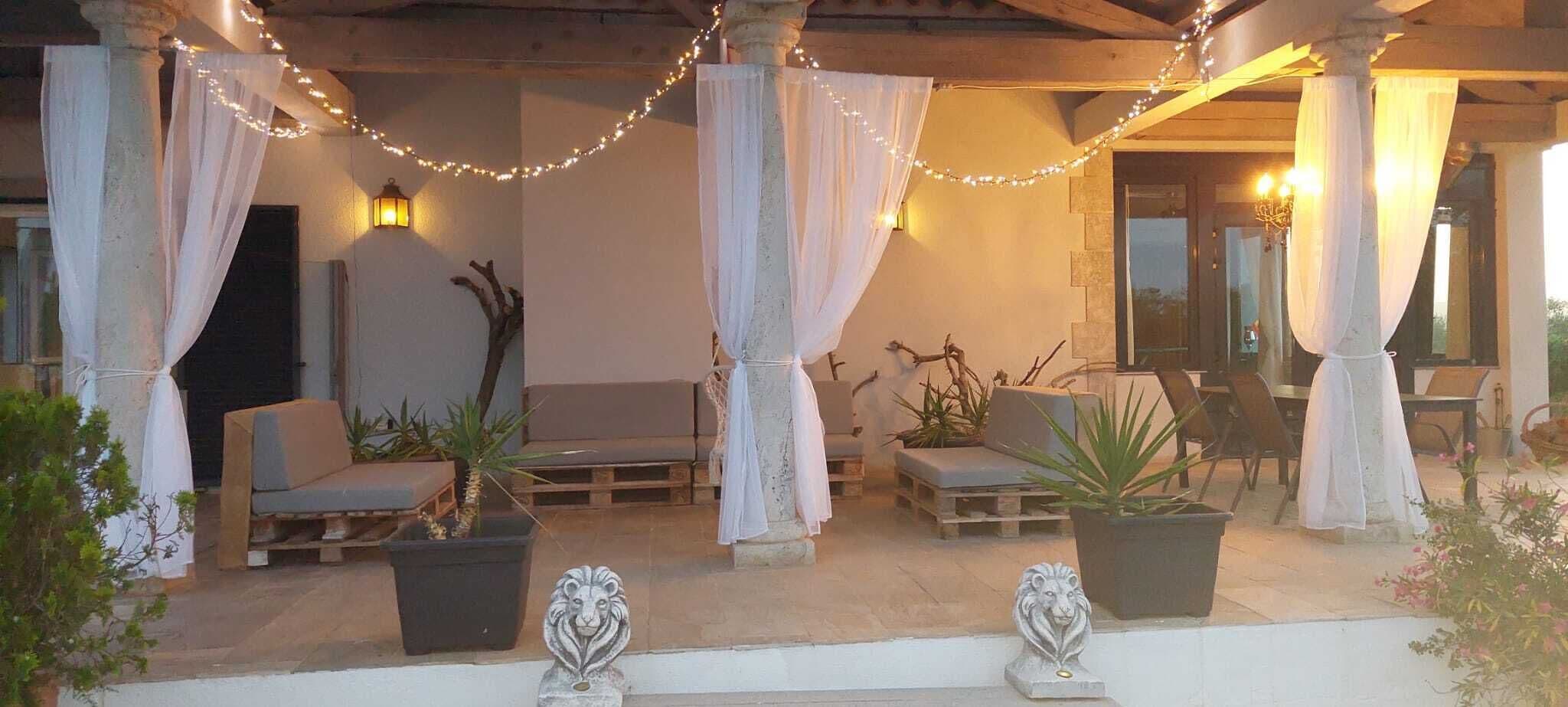 An outdoor seating area with chairs and potted plants, draped with white fabric and string lights.