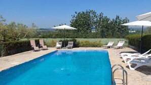 Ein Swimmingpool mit Liegestühlen und Sonnenschirmen, umgeben von Grünpflanzen und mit Blick auf ferne Hügel.
